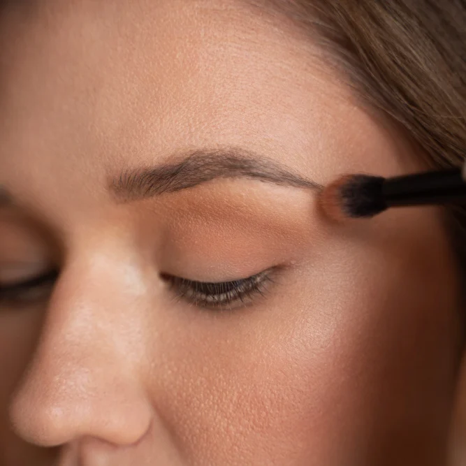 Frau appliziert Augenbrauen-Make-up mit einem Pinsel.