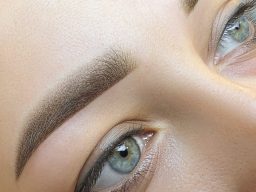 Nahaufnahme eines Gesichts mit betonten Augenbrauen und leuchtenden grünen Augen.