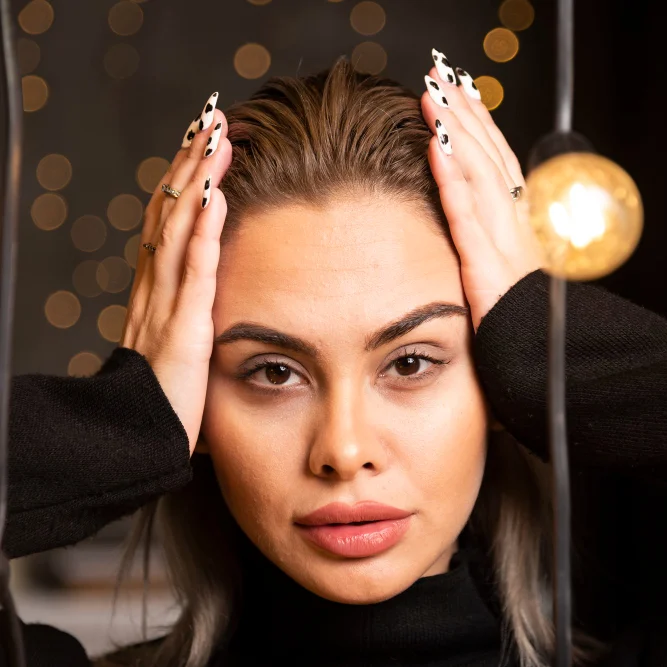 Junge Frau mit gestyltem Haar, die ihre Hände auf den Kopf legt, sieht besorgt aus.