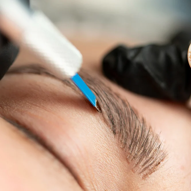 Nahaufnahme eines Augenbrauen-Designs mit einer feinen Nadel und präziser Handbewegung.